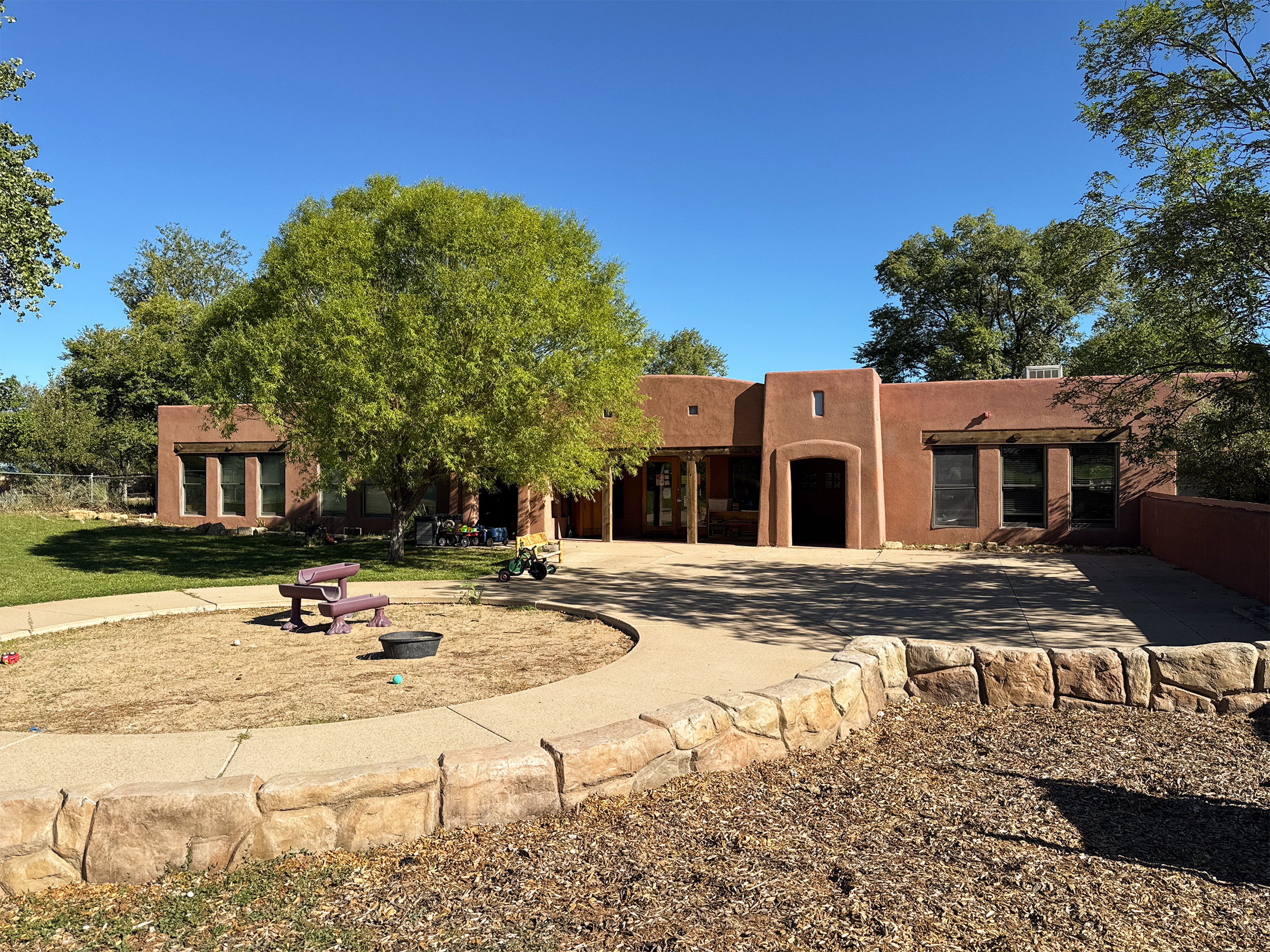The front of the Children's Kiva Preschool. The image shows the front of the school and one of 2 playgrounds. 